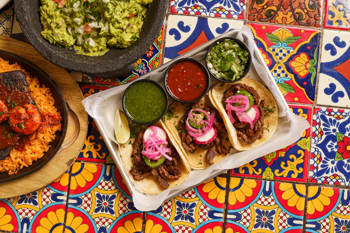 Plateau de tacos al pastor posé sur des carreaux de talavera multicolores, entouré de salsas et de guacamole